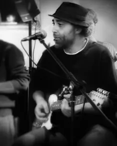 Schwarz-Weiß-Foto des Musikers Yassine Karoui, der singt und Gitarre spielt