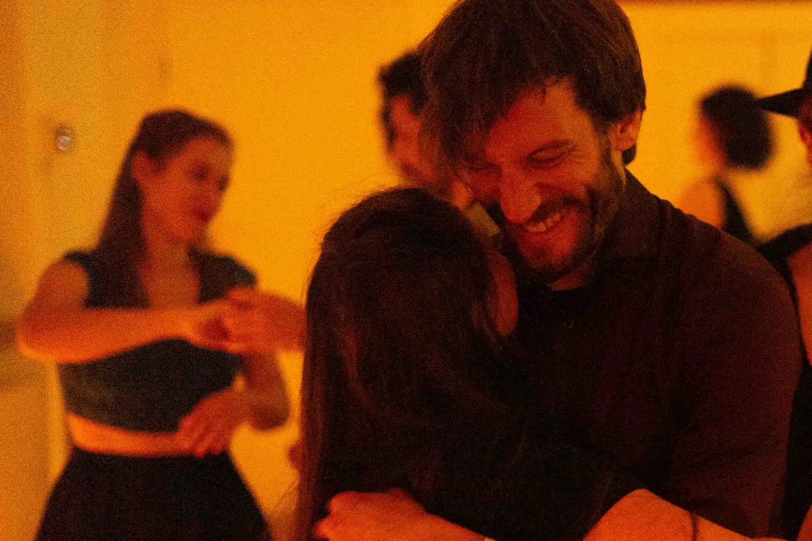 Ein lächelnder bärtiger Mann hält seine Partnerin beim Blues-Tanz in warmem orangem Licht eng umschlungen