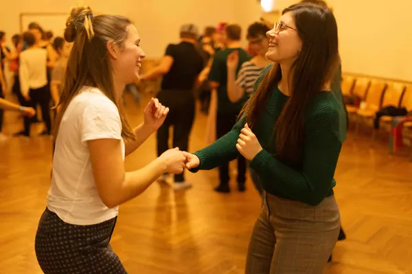 Blue Forest 2023: Zwei lachende Frauen tanzen Hand in Hand in einem golden beleuchteten Tanzsaal
