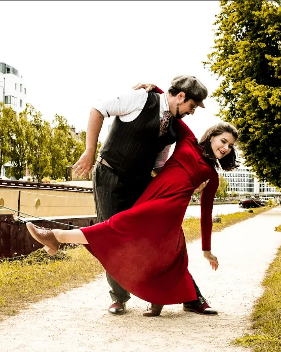 Die Lehrer Alina & Nicolas in einer dramatischen Pose auf einem Uferweg, sie im roten Kleid